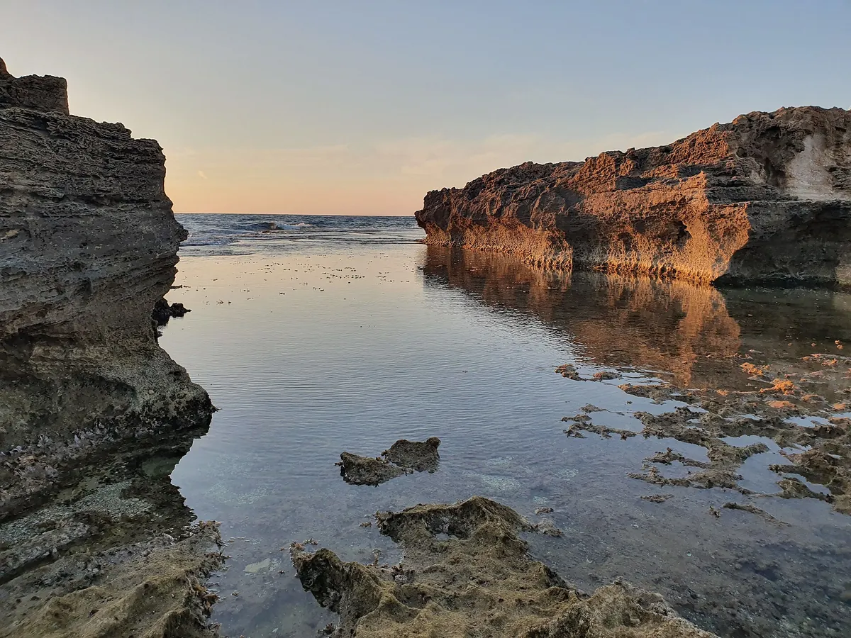 Calm water in a rocky inlet of the Dor-HaBonim beach reserve, with sandstone cliffs lit by the evening sun