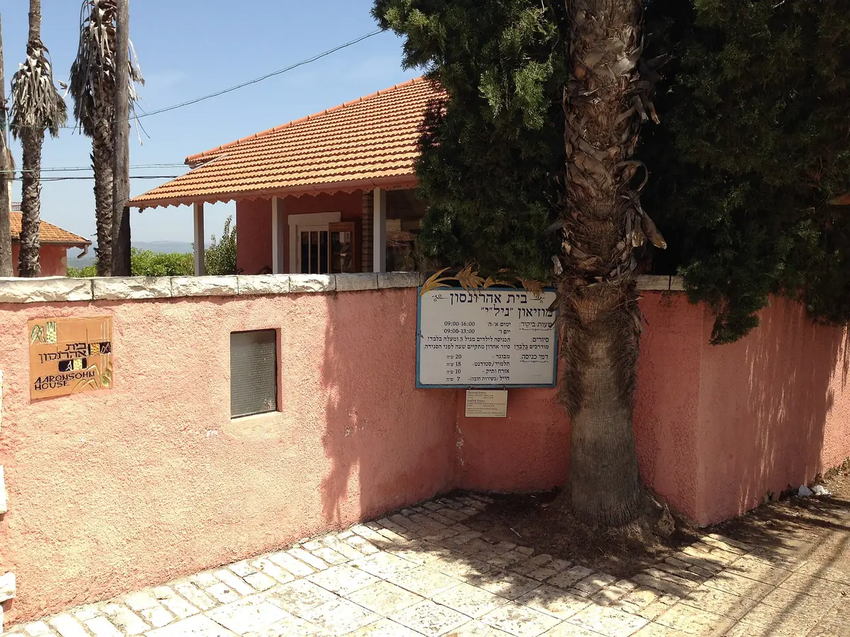 The pink garden wall and gate of Beit Aaronsohn, the NILI museum, with a sign and a tiled roof behind
