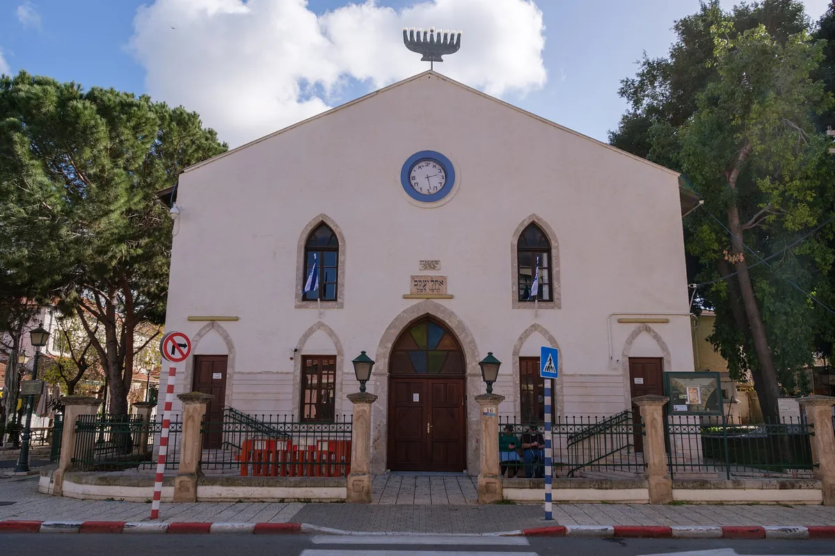 Front of the Ohel Yaakov synagogue (1886): a pale gabled facade with arched windows, a round clock and a menorah on the roof