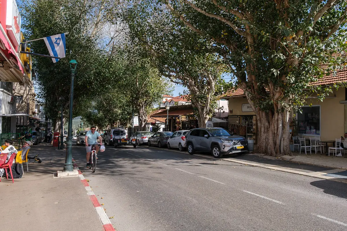 A tree-lined street in the centre of Zichron Yaakov with low old houses, cafe tables and an Israeli flag